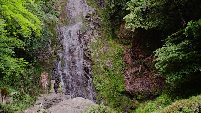 新緑の岩肌をダイナミックに流れ落ちる清水の滝と傍らに佇む石仏（佐賀県）