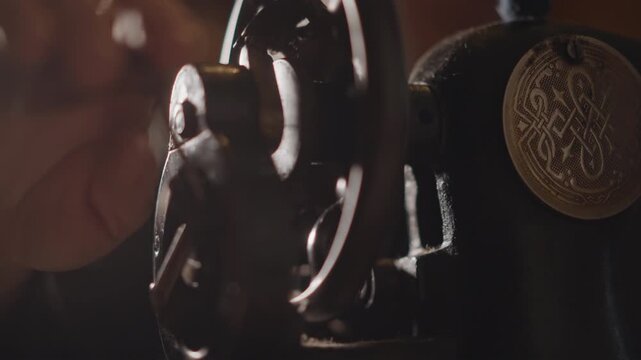 Woman examines ornate machine. Woman adjusts vintage sewing device. Female inspects decorative sewing machine wheel carefully. Woman carefully examines detailed antique sewing machine part
