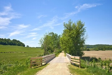 Fototapeta premium View of a wooden bridge along the Heritage Trail between lush green fields on a sunny spring day in Dubuque County, Iowa.