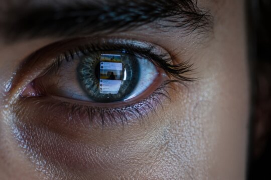 Extreme close up of human eye reflecting endless smartphone feed with digital content in pupil, screen addiction concept, online attention economy, social media scrolling, technology dependence.