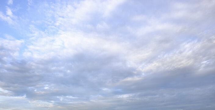 Soft white altocumulus clouds across peaceful bright blue sky background