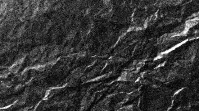 Dark rough textured surface resembling crumpled paper or dark grey slate stone with dramatic lighting and shadows, 4k video