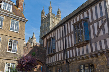 Obraz premium Historic half-timbered buildings frame a view of Gloucester Cathedral's impressive tower against a clear blue sky