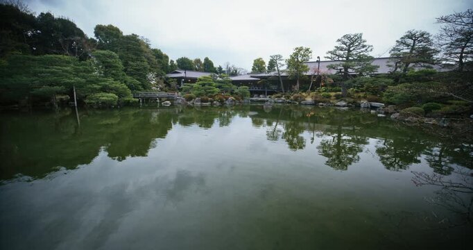 Reflective Japanese pond with surrounding structures and trees - wide shot