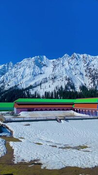 Breathtaking winter landscape of Malam Jabba Swat Valley Pakistan with snow-covered mountains and colorful resort buildings under a clear blue sky.