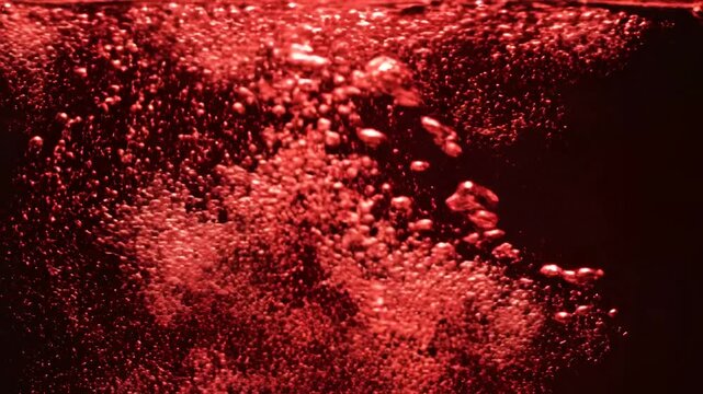 Closeup of Red Bubbles Rising in Dark Liquid.
