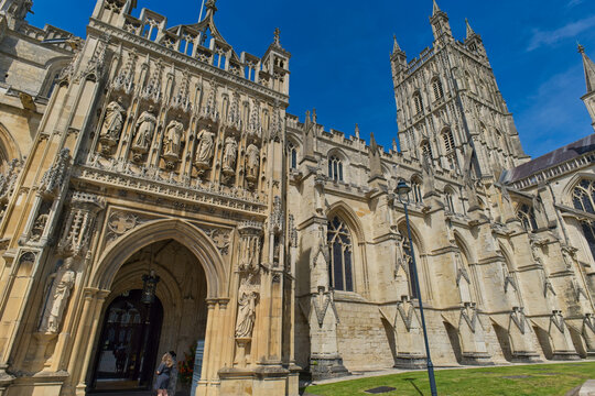 A grand, ornate stone cathedral exterior stands under a clear blue sky. Intricate carvings adorn the main entrance at Gloucester Cathedral - Gloucester - Gloucestershire - UK
