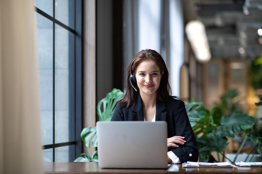 Attractive business woman Asian in suits and headsets are smiling while working with computer at office. Customer service assistant working in office. VOIP Helpdesk headset
