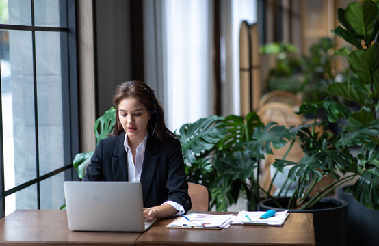 Attractive business woman Asian in suits and headsets are smiling while working with computer at office. Customer service assistant working in office. VOIP Helpdesk headset