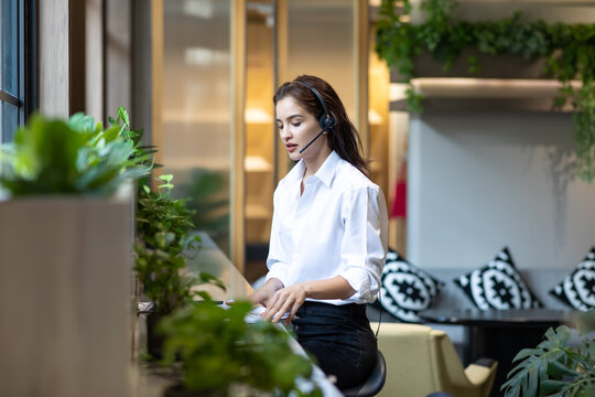 Attractive business woman Asian in suits and headsets are smiling while working with computer at office. Customer service assistant working in office. VOIP Helpdesk headset