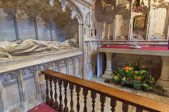 An ornate stone effigy lies on a tomb within a historic chapel, featuring Gothic architecture and a floral display at Gloucester Cathedral - Gloucester - Gloucestershire - UK