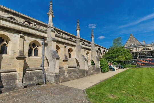 A long stone building with Gothic arches and pinnacles stands beside a sunny green lawn at Gloucester Cathedral - Gloucester - Gloucestershire - UK