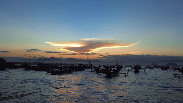 Sunrise over tropical bay with local fisherman boats silhouette, scenic golden hour sky and lenticular cloud landscape for travel video. Papuma Beach, Jember, Indonesia