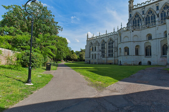 A paved path next to a grand, light-colored Gothic-style building, green lawn, and distant trees under a clear sky at Gloucester Cathedral - Gloucester - Gloucestershire - UK