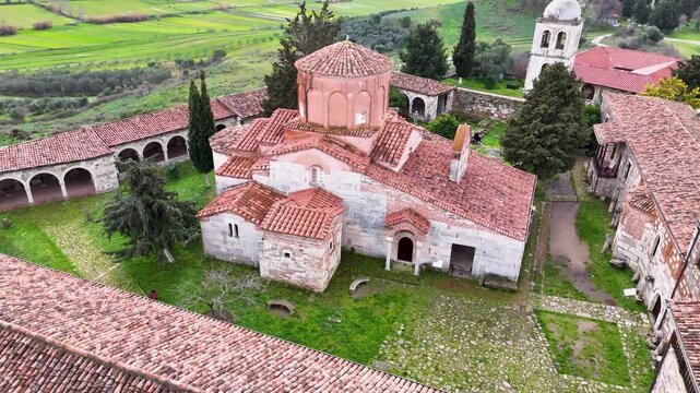High-angle aerial shot circling the historic Byzantine brick domes, weathered red tile roofs, and grassy interior courtyard of St. Mary Church at Apollonia Archaeological Park, Albania