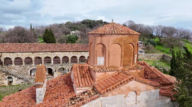 Aerial circle orbit shot around the 13th-century Byzantine Church of St. Mary in Apollonia Archaeological Park, Albania, showcasing its red brick dome and ancient stone cloister courtyard