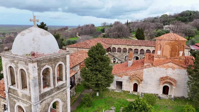 Aerial push-in shot moving toward the historic 13th-century St. Mary Monastery and its iconic stone bell tower at the Apollonia archaeological site in Fier, Albania