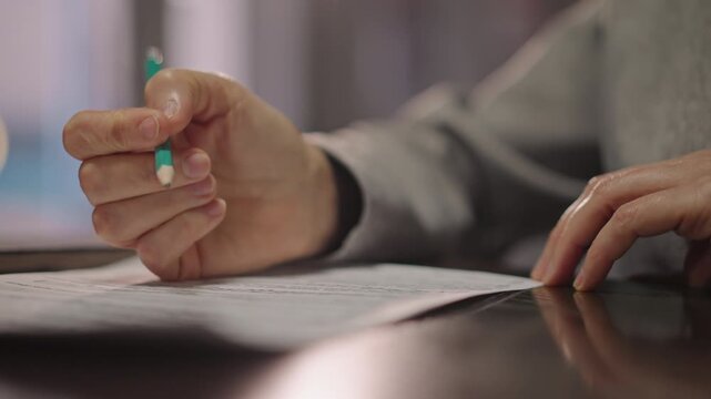 Closeup hands marking sheet music on polished desk, instructor annotating notation with green pen, soft warm lighting, calm focused mood, visible paper texture and reflective surface, detail shot