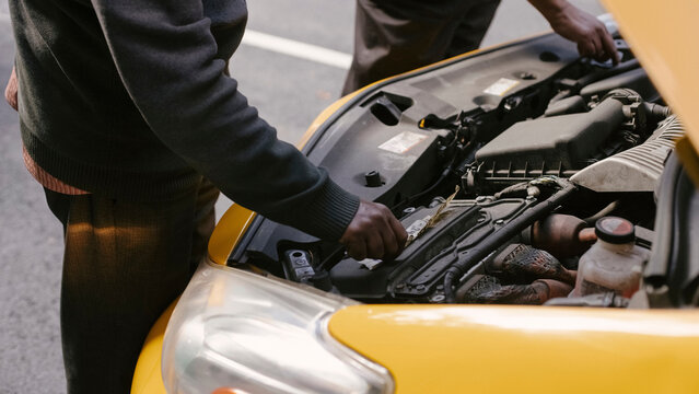 Mechanics inspect open hood engine bay of yellow taxi on city street