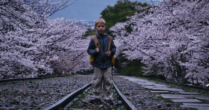 Wide shot of child with backpack on rail surrounded by spring cherry blossom trees at dusk