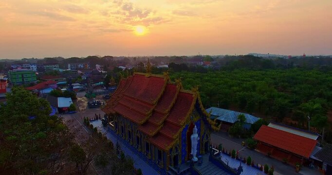 Aerial view of Wat Rong Suea Ten, the famous Blue Temple in Chiang Rai, Thailand, featuring stunning blue architecture illuminated by the warm glow of sunrise. Ornate Blue Church and Stupa at Sunrise