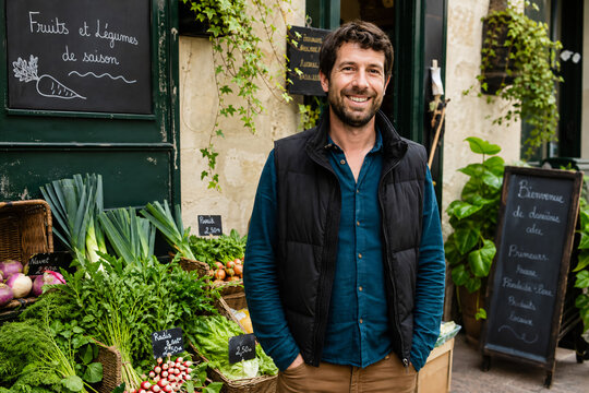 Commer&ccedil;ant fran&ccedil;ais souriant devant sa boutique de fruits et l&eacute;gumes