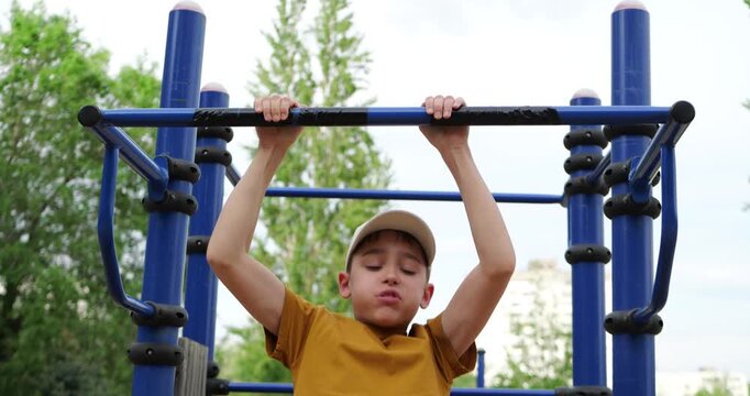 Child performs pull-ups on playground equipment. Young boy strengthens muscles in outdoor park. Active lifestyle promotes health and fitness for kids.