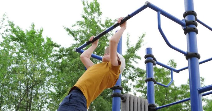 Upset child jumping down from pull-up bar after unsuccessful attempt on outdoor playground. Emotional childhood scene captures struggle, disappointment and effort during fitness activity.