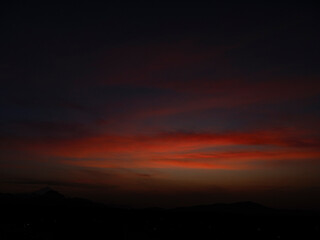 Fototapeta premium Oscuro cielo de crepúsculo con nubes rojas intensas y silueta de montañas en el horizonte