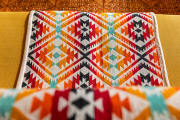 Yellow sofa decorated with colorful indigenous handmade blanket in a cozy living room interior. Cozy home styling with traditional Andean textile runner on a modern couch.