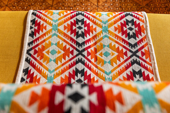 Yellow sofa decorated with colorful indigenous handmade blanket in a cozy living room interior. Cozy home styling with traditional Andean textile runner on a modern couch.