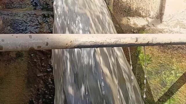 Close-up shot of liquid flocculant chemical continuously dripping and dosing into a stream of flowing raw water for purification.