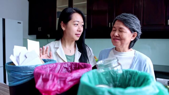 Asian daughter teaching her elderly mother how to sort trash for recycling at home