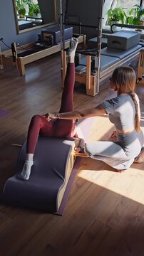 Woman doing exercises on back spine corrector with trainer. Reformer pilates studio machine for fitness workouts in gym. Fit, healthy and strong authentical body. Fitness concept