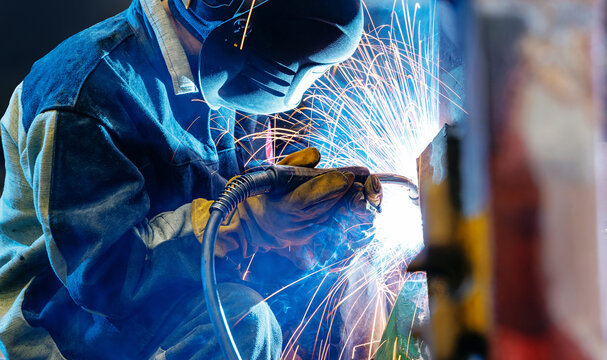 Welder performing shielded welding with sparks in factory, recovery work for excavator bucket