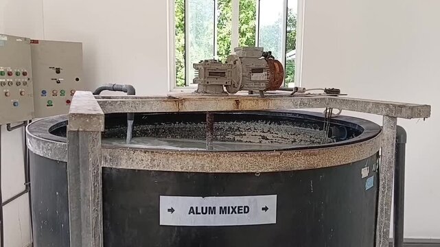 A mechanical agitator stirring an Alum or PAC chemical solution inside a large dark tank at an industrial water treatment facility.