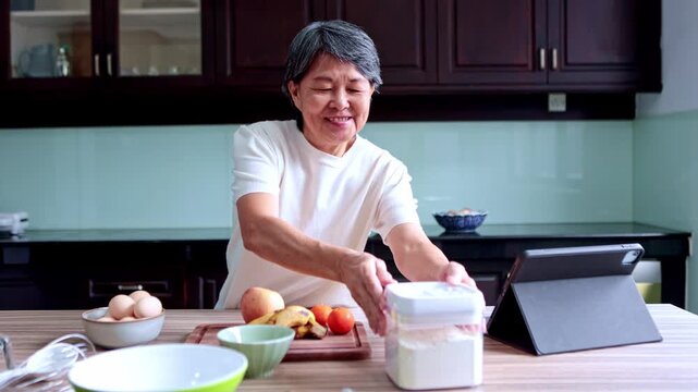 Elderly asian woman learning to cook online in her kitchen