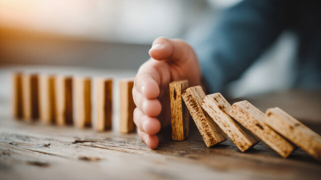 Hand stopping falling wooden blocks on a table during playtime in a bright indoor space with natural light in the afternoon