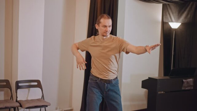 Male instructor directs acting movement exercise in studio with upright piano, partner improvisation, reaching gestures, responsive student interaction, focused posture work, warm lighting