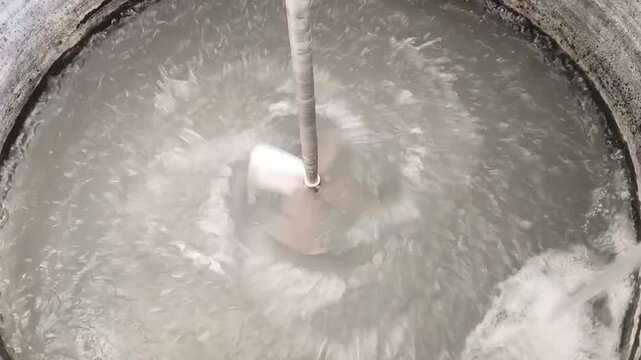Top view of an industrial agitator rotating to mix water inside a large chemical mixing tank during the water treatment process.