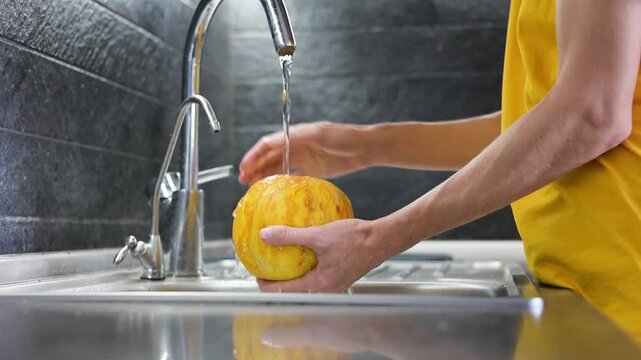 Person washing ripe yellow melon under running water in kitchen sink video Full HD