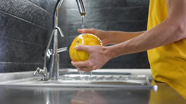 Person washing ripe yellow melon under running water in kitchen video Full HD sink