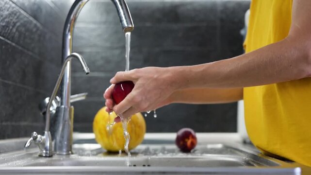 Washing ripe red plum under running water in kitchen sink at home video Full HD