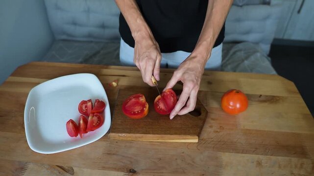 Person slicing fresh red tomato on wooden board and arranging pieces on Full HD plate video