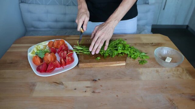 Woman slicing fresh herbs beside vegetables on kitchen table Full HD video