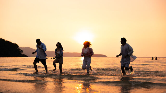 Family summer vacation concept. Happy family running and splashing in shallow sea water at sunset on a tropical beach. Togetherness, freedom, travel, leisure, happiness