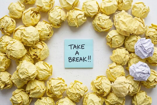 Writer's Block and Burnout Concept: "Take a Break" Sticky Note Surrounded by Crumpled Yellow Paper Balls on White Background