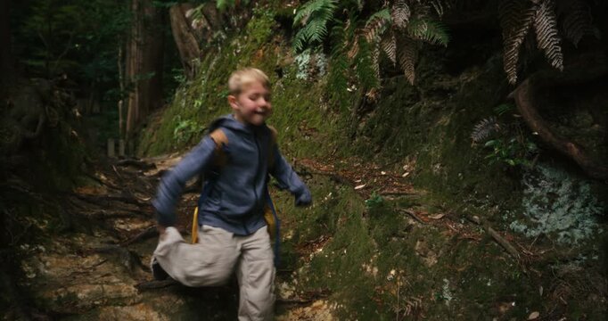 Little boy with backpack hiking down hill in Japanese woods - steady cam shot
