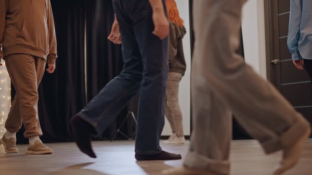Studio rehearsal with white students walking across stage under soft lights, acting coach directing blocking and footwork, casual clothing and sneakers, black curtains and spotlight, collaborative