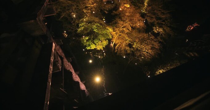 Steady cam movement looking over edge of ancient Japanese temple to glowing trees below
